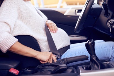 cropped up of pregnant woman driving the car, buttoned up with seat belt