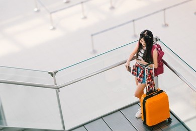 cute teenage asian traveler girl, college student using smartphone call or chat at airport with luggage, backpack. web check in, lonely travel study abroad, or international tourism lifestyle concept.