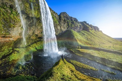 tourist standing in front of seljalandsfoss one of the best known waterfalls in southern iceland, the most famoust icelandic waterfall , beautiful amazing landscape from iceland,
