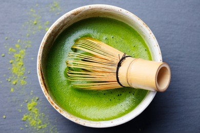 matcha green tea cooking process in a bowl with bamboo whisk. black slate background. top view.