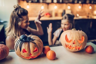 happy halloween! attractive young woman with her little cute daughter are preparing to halloween on kitchen. mom with daughter are having fun with pumpkins.