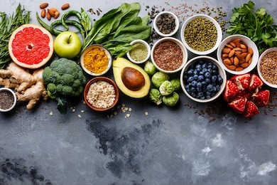 healthy food clean eating selection: fruit, vegetable, seeds, superfood, cereals, leaf vegetable on gray concrete background copy space