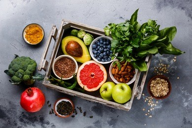healthy food clean eating selection in wooden box: fruit, vegetable, seeds, superfood, cereals, leaf vegetable on gray concrete background