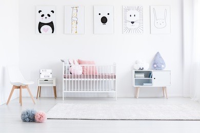 girl's bedroom with pastel pompons on floor and pink pillows on bed against wall with drawings