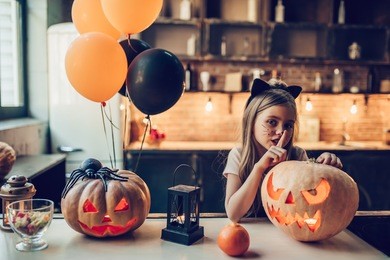 happy halloween! little cute girl is preparing for halloween. having fun with pumpkins on kitchen with cat halloween makeup.