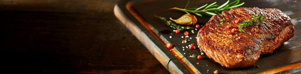 piece of cooked rump steak with spices served on wooden cutting board