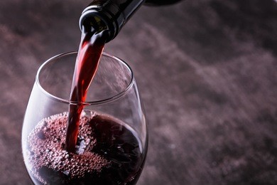 pouring red wine into the glass against wooden background