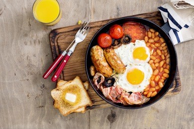 full english breakfast in a cast-iron frying pan on a wooden light table with copy space, top view