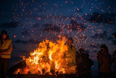 large burning bonfire with soft glowing flame and sparkles flying all around. romantic summer evening, people relaxing and enjoying calmness at the seaside during the night of ancient lights