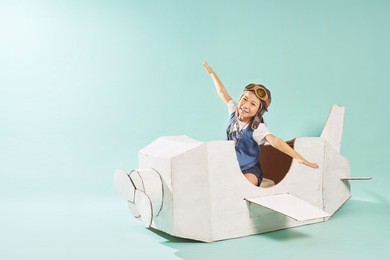 little cute girl playing with a cardboard airplane. white retro style cardboard airplane on mint green background . childhood dream imagination concept .