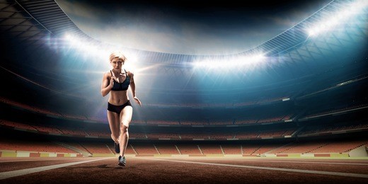 young woman running on racetrack. illuminated night track and field stadium.