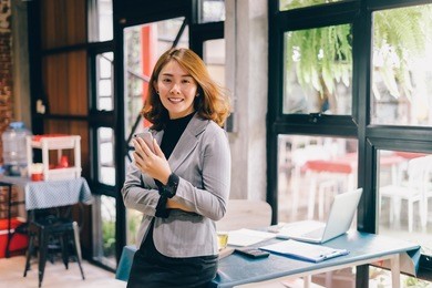 smiling business woman working in office with documents,happy asian businesswoman using phone sitting on chair at modern home studio.concept of young people working mobile devices,contact to costumer