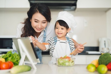 mother with her daughter preparing lunch in the kitchen and enjoying together.