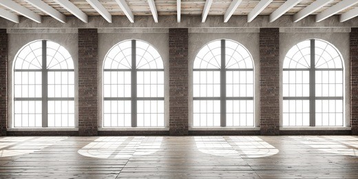 large empty room in loft style with big arched windows illuminated by sunlight.interior mock up with wooden floor and brick wall. 3d render.