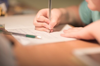close up kid's hand writing on paper, writing messy math on wooden table in room,student child girl holding pen doing homework at home, education concept.