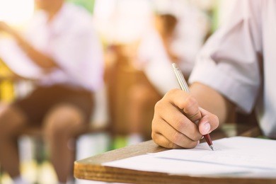 closeup to hand of student  holding pen and taking exam in classroom with stress for education test.vintage style