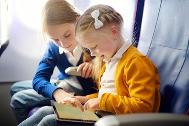 adorable little girls traveling by an airplane. children sitting by aircraft window and using a digital tablet during the flight. traveling abroad with kids.