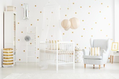 decor pillow on grey armchair in bright newborn baby's interior with lanterns above bed