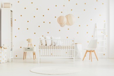 pastel lanterns above newborn baby's bed in bright bedroom with white chair and cabinet