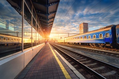 beautiful train with blue wagons at the railway station at sunset. industrial view with modern train, railroad, railway platform, buildings, sky with clouds in sunny evening. railway tourism. vintage