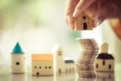 woman's hand putting house model on coins stack. concept for property ladder, mortgage and real estate investment .