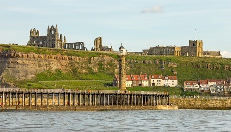 st mary's church and the ruins of whitby abbey on top of the east cliff, whitby with whitby lighthouse in the foreground, taken from the sea