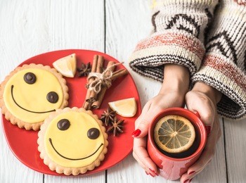red cup of hot tea with lemon in hands of the girl in the sweater,on a white wooden background red and a plate of cookies,the concept of hot drinks
