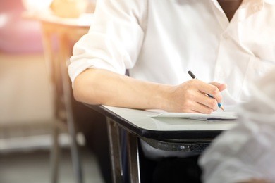 soft focus.high school or university student holding pencil writing on paper answer sheet.sitting on lecture chair taking final exam attending in examination room or classroom.student in uniform.