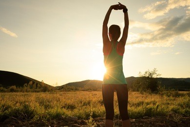 trail runner woman stretching arms before run on sunset forest