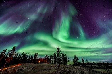 amazing aurora in purple and blue color dancing over chalet in yellowknife