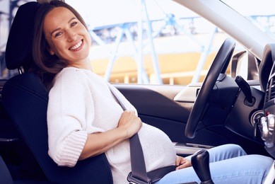 side view of joyful pregnant woman posing on driver seat in car 