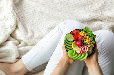 girl in white jeans holds in hands fork, vegan breakfast meal in bowl with avocado, quinoa, cucumber, radish, salad, lemon, cherry tomatoes, chickpea, chia seeds. top view, copy space. clean eating.