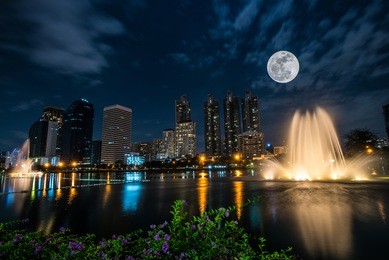 view of city park, beautiful fountain, night light and full moon with high-rise at sukhumvit business area, bangkok, thailand.