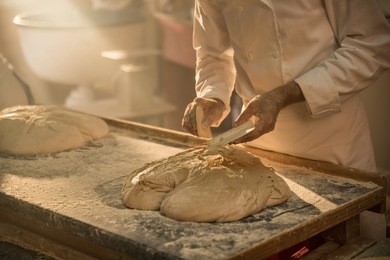 in an artisan bakery, a baker prepare the bread dough. the morning sun comes in through the window