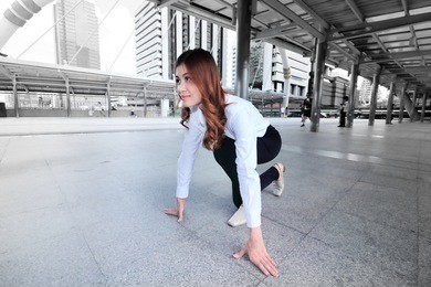 wide angle shot of attractive young asian woman in start position ready to run at urban city background. competition business concept. low key toned image