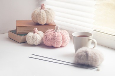 autumn cozy window composition, window at home. book, cup, needles, yarns ball and knitted pumpkins, toned photo