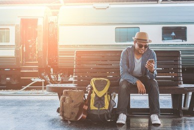 young handsome man sitting and using smartphone at train station