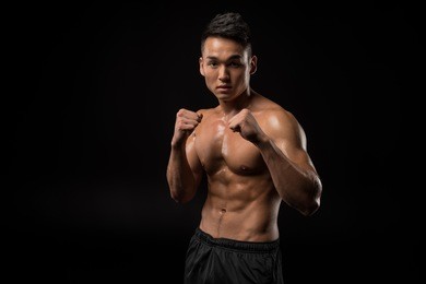 shirtless asian sportsman boxing and looking at camera isolated on black