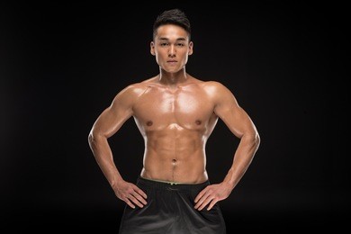 shirtless muscular asian man standing with hands on waist and looking at camera isolated on black