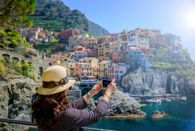 female tourist person taking photo with smartphone by famous coast of italy; manarola of cinque terre in spring time