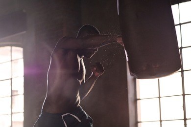 an afro-american guy trains in a vintage gym and fists his boxing bag fists. concept of: gym, fitness, boxing, success, workout and power