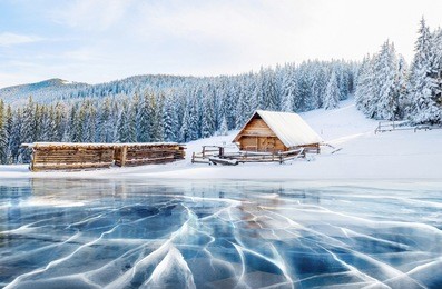cracks on the surface of the blue ice. frozen lake in winter mountains. it is snowing. the hills of pines and cabin in the mountains. mysterious fog. carpathians ukraine