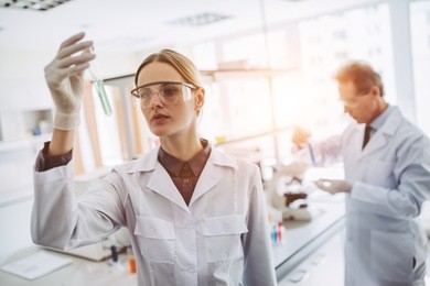 two scientists are working in laboratory. young female researcher and her senior supervisor are doing investigations with test tubes.
