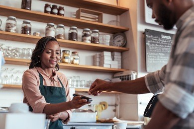customer using a bank card and nfs technology to pay a barista for a purchase at a cafe