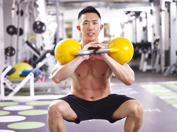 asian male bodybuilder working out in gym using kettle bells.