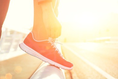 cropped shot view of young fit woman tie shoelaces while standing on a road during jogging in summer evening, sporty girl tying the laces on running shoes while taking break between training outside