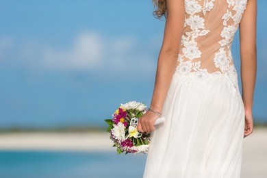 beautiful bride walks on the beach with bouquet of flowers. woman in long white dress. female turned her back.