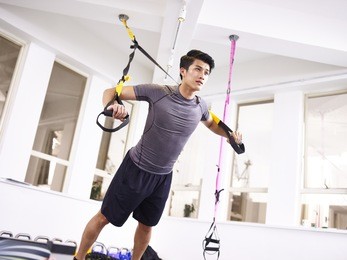 young asian man exercising in gym using fitness straps.