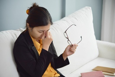 tired asian glasses woman rubbing eyes and sitting on white sofa. copy space. illness, exhausted from overtime working concept.