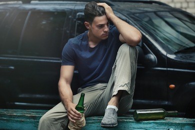 man sitting with bottle of alcohol near car
